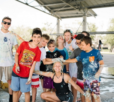 Campers gather around activity leader and smile after a messy and wet game at the plaza
