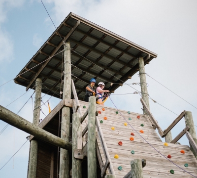 Camper and activity leader look out over the rest of the challenge course after a climb up the rockwall.
