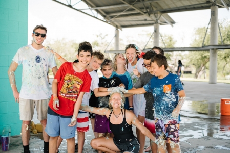 Campers gather around activity leader and smile after a messy and wet game at the plaza