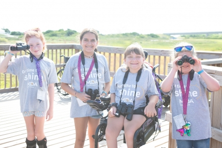 Four campers from Camp MDA smile and show off binoculars in the middle of birdwatching. Photo by: Beyond Memory Photography